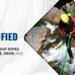 A man is standing on a icy, snow rock with the help of dry treated climbing rope